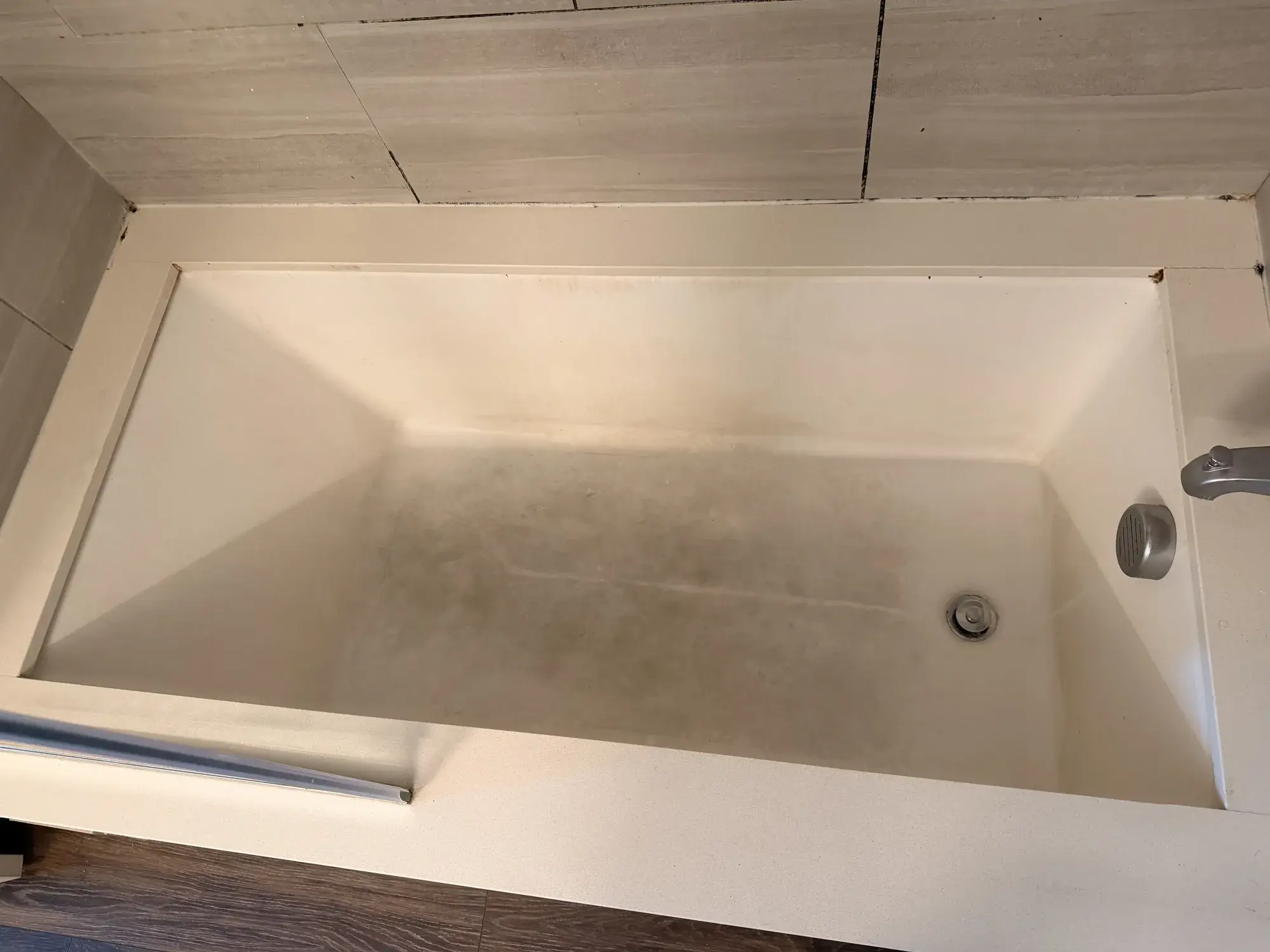 Bathtub before refinishing, worn finish in a modern stone-tile bathroom